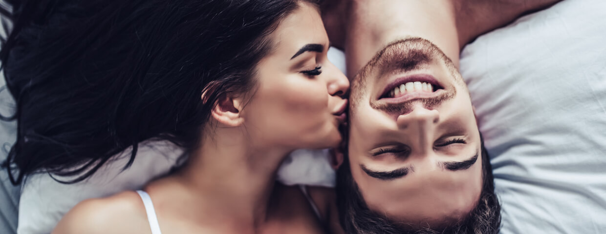 woman kissing her partner on the cheek in bed