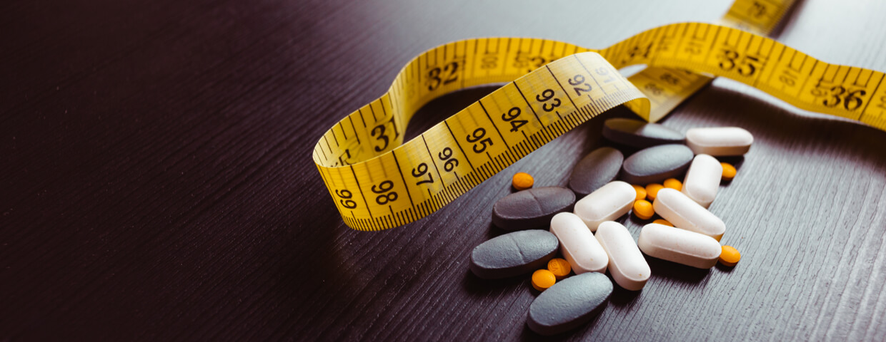 Many different weight loss pills, or appetite suppressants, and supplements, with measuring tape on black wooden table. Diet pills and supplements, prescription weight loss drugs. 