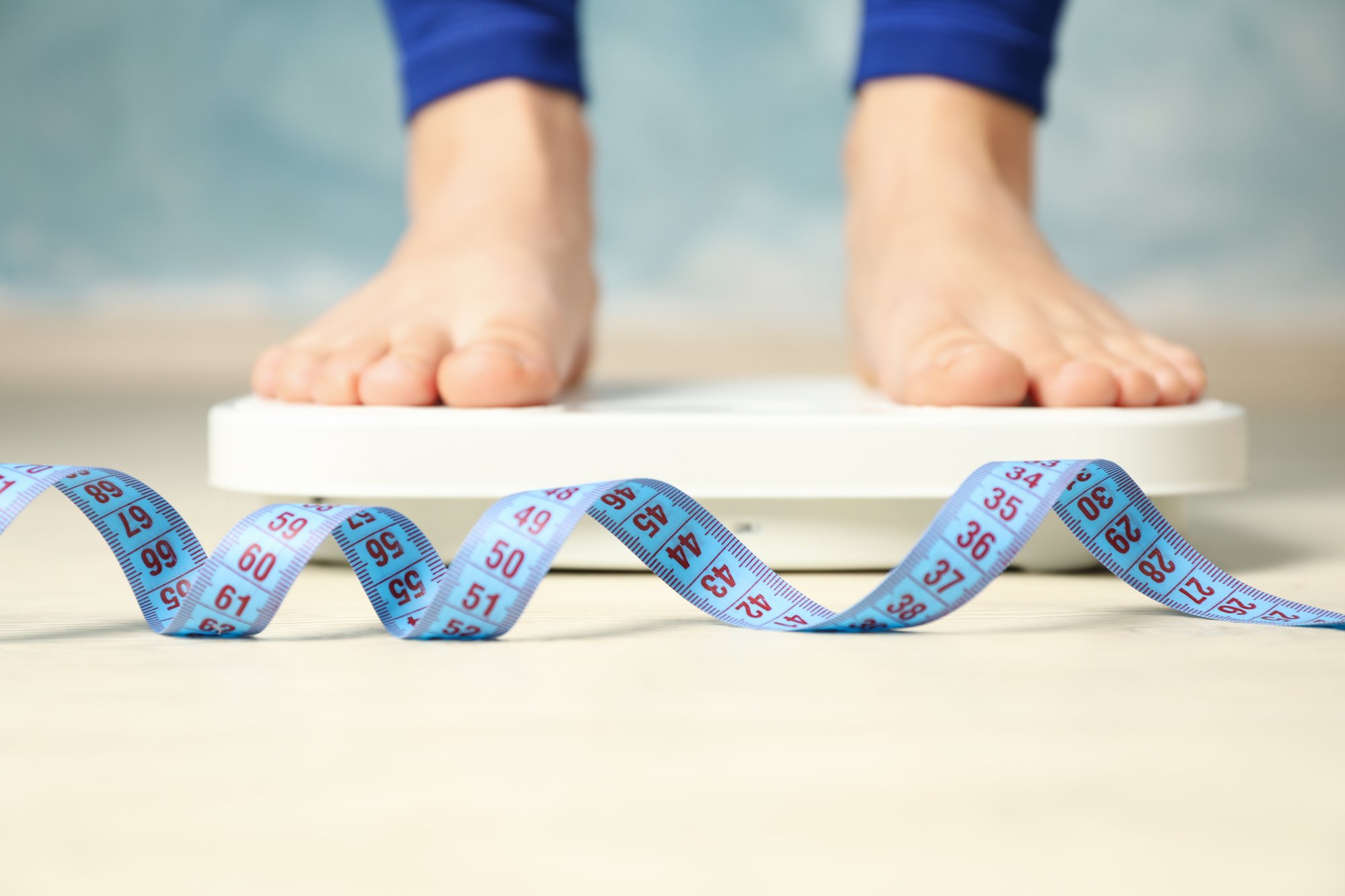 Feet on a scale in the background and a curly blue measuring tape in the foreground