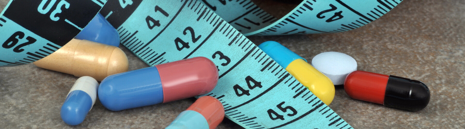 various pills on a counter top with a blue measuring tape