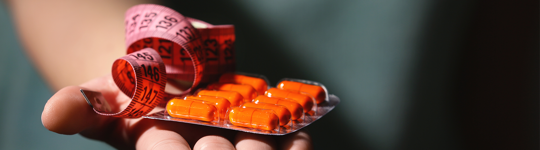 red measuring tape with orange pills in hand