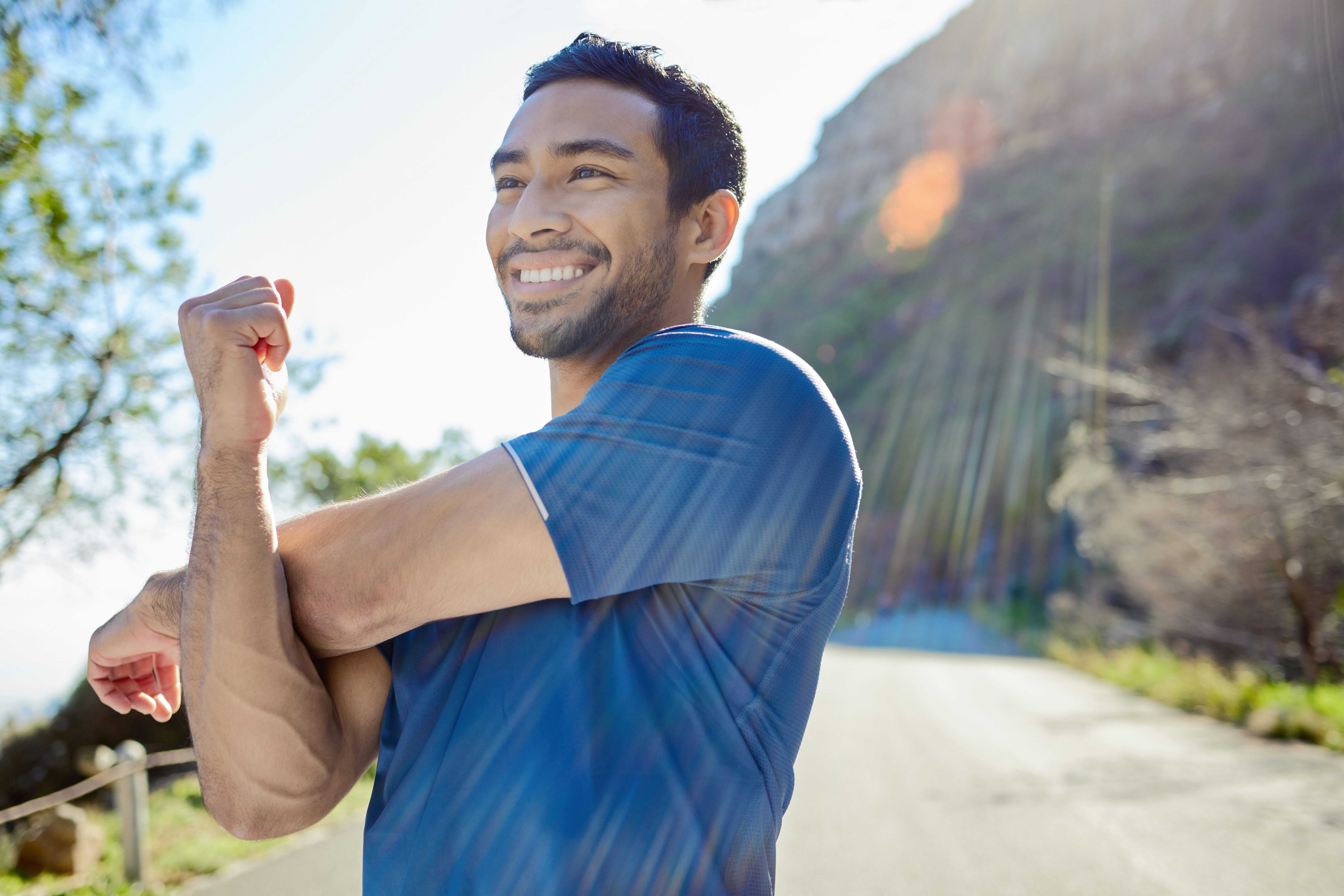 A healthy man stretches his arms while out for a hike in the bright sunlight
