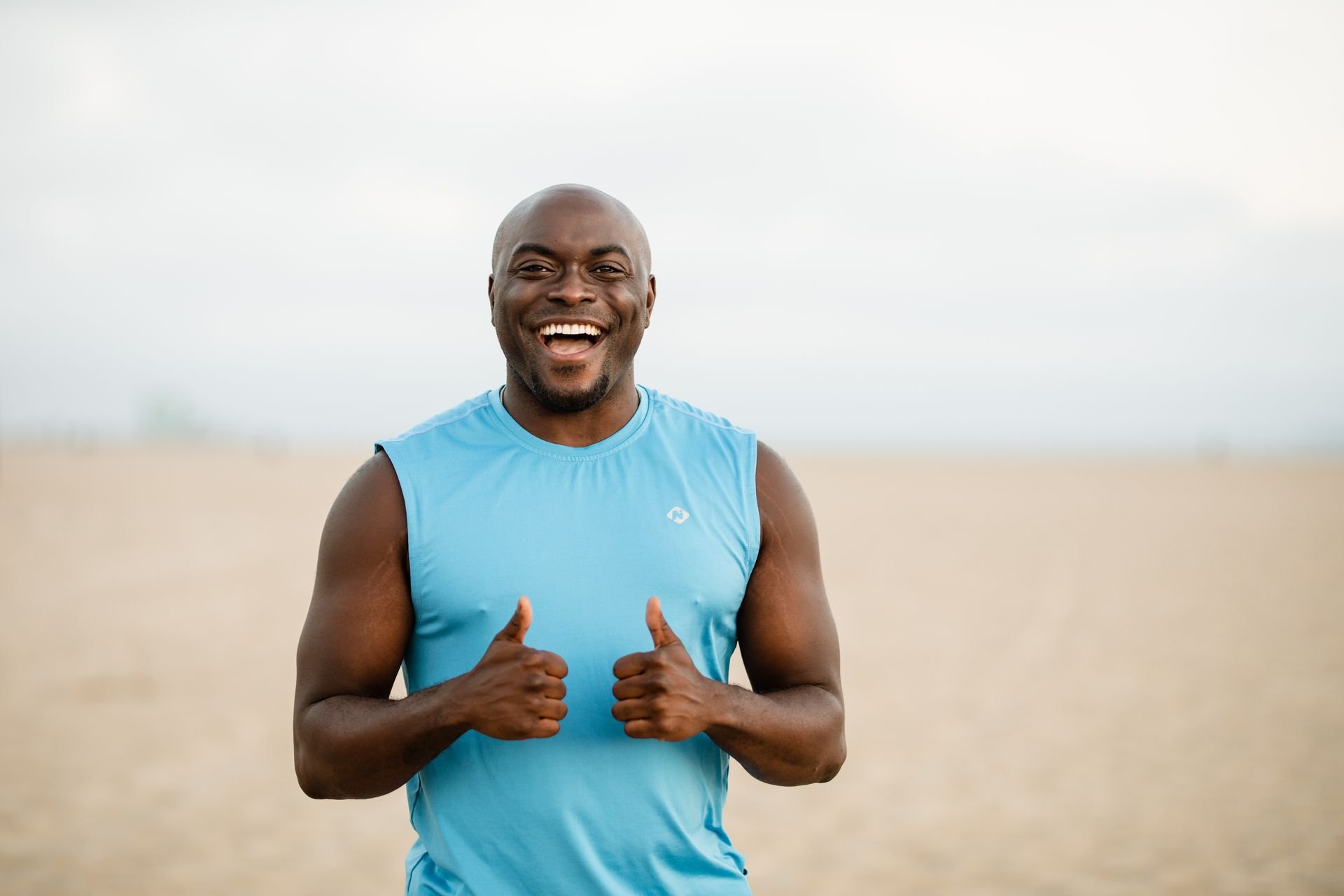 a happy man in a blue sleeveless shirt doing a thumbs up